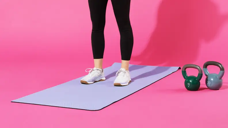 Person standing on top of purple lululemon 5mm workout mat in running sneakers, next to kettlebells.