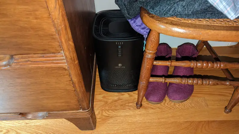 Small air purifier placed on floor next to chair, shoes and dresser.