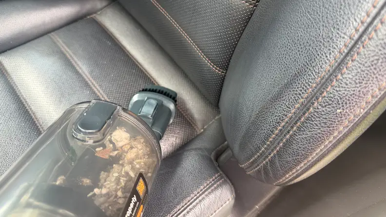 Handheld piece of Yaber HP20 cordless vacuum being used to clean black leather seat of a car.