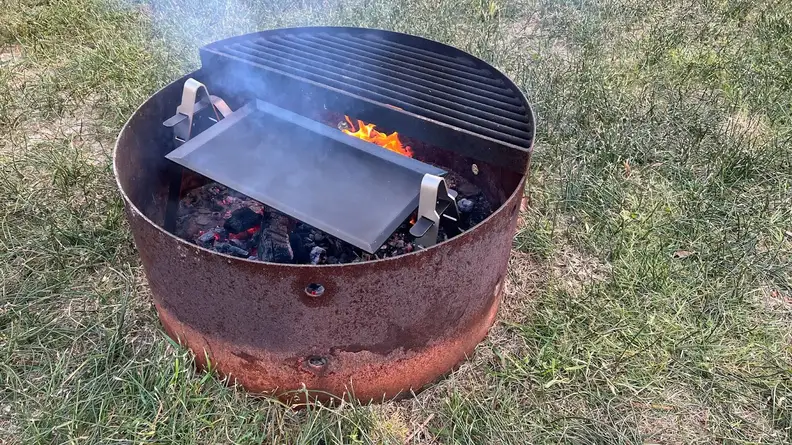 Made In Carbon Steel Griddle cooktop inside of fire pit with open flame.