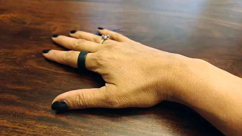 Circular Ring Slim and a wedding ring on fingers of a hand on a wooden table