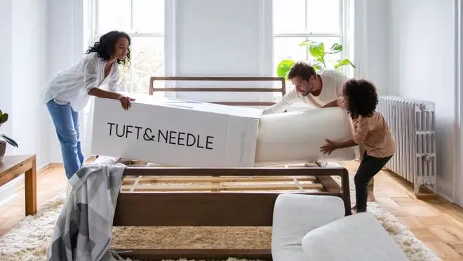 Three people assembling mattress together in bedroom.