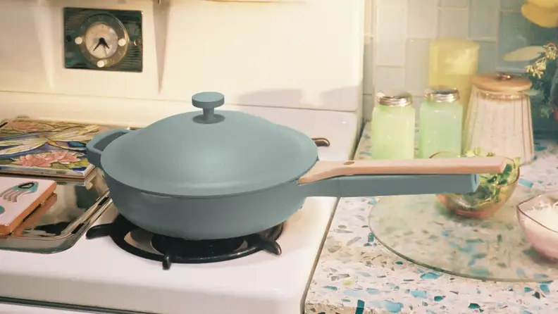 A light blue pan with a lid sits on a gas stovetop in a modern kitchen.