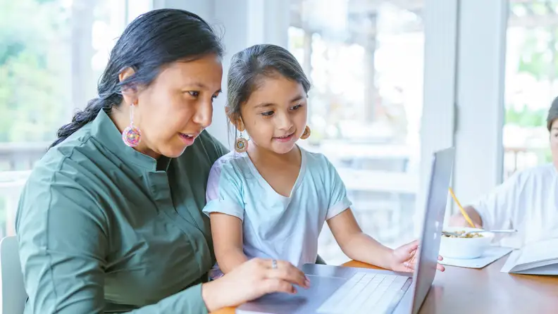 A parent and a child browsing on a laptop.