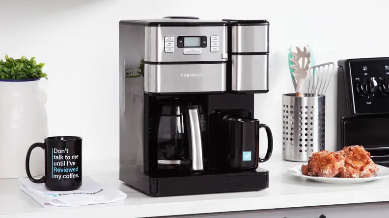 The silver and black Cuisinart coffee machine on a counter next to a coffee mug and plate of pastries.