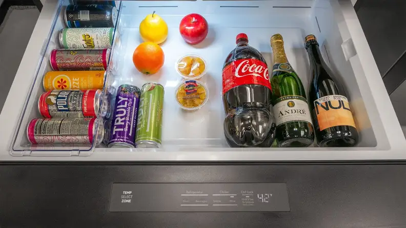 A close-up of the interior of the flex drawer. Its interior is a large, open area with a can organizer along its left edge. The drawer's contents include small snacks and beverage containers of varying size, including cans, wine bottles, and a 2-liter bottle of soda.