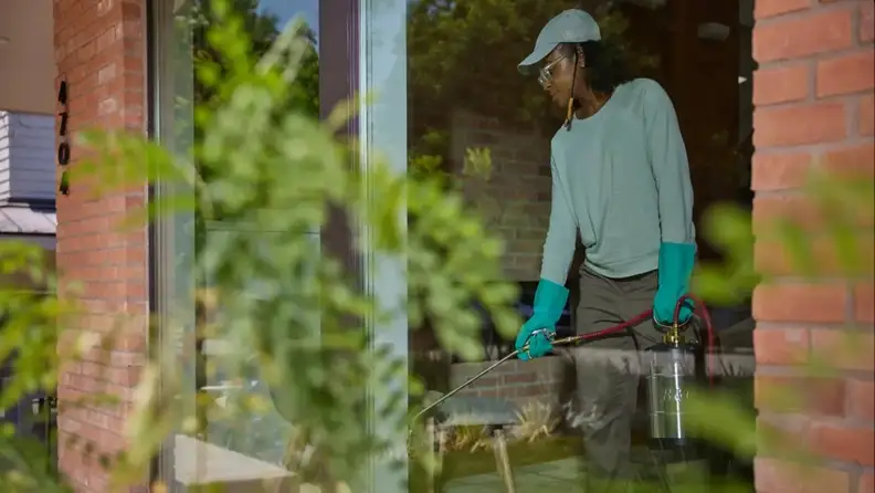 Technician spraying pesticide near entryway with sprayer tank
