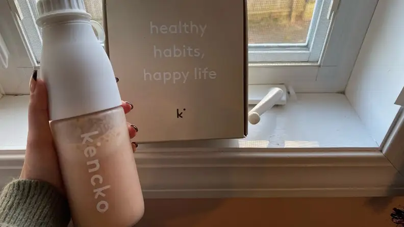 Person holding smoothie bottle in front of box packaging.