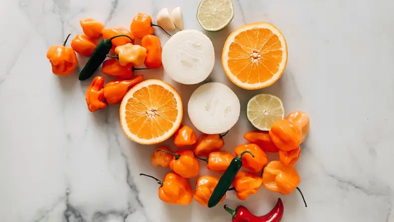 Oranges, peppers, and onions arranged artfully on a marble surface.