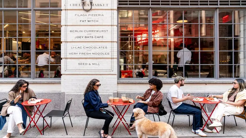 People dining at outdoor tables in front of Chelsea Market's storefront sign