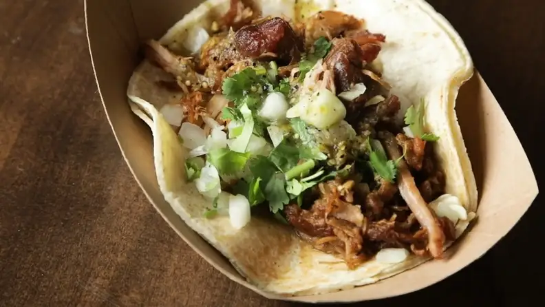 A pork taco topped with onion, cilantro, and salsa verde