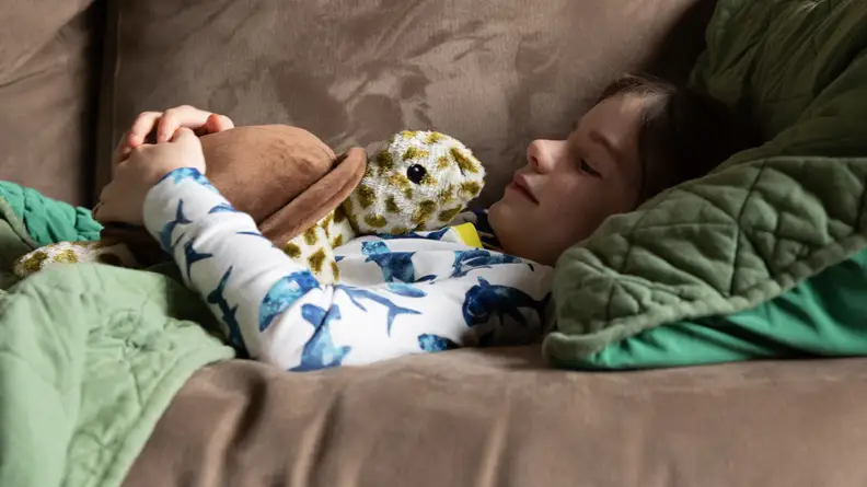 A child lays down with a turtle Warmies on their chest.