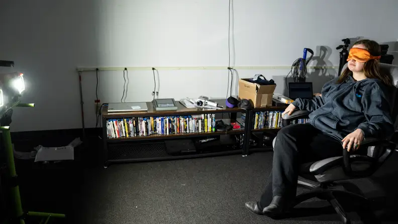 sara sits in a chair in a dark room wearing the loftie mask with a floodlight on her