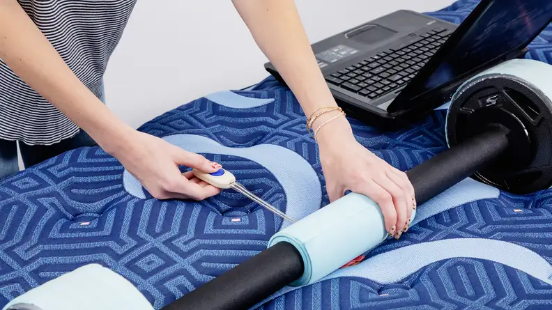 A person measuring the pressure underneath a barbell resting on a mattress.