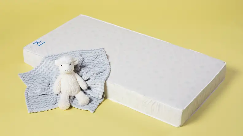 A Delta Children Twinkle Stars crib mattress on a yellow background with a stuffed animal and baby blanket on top.