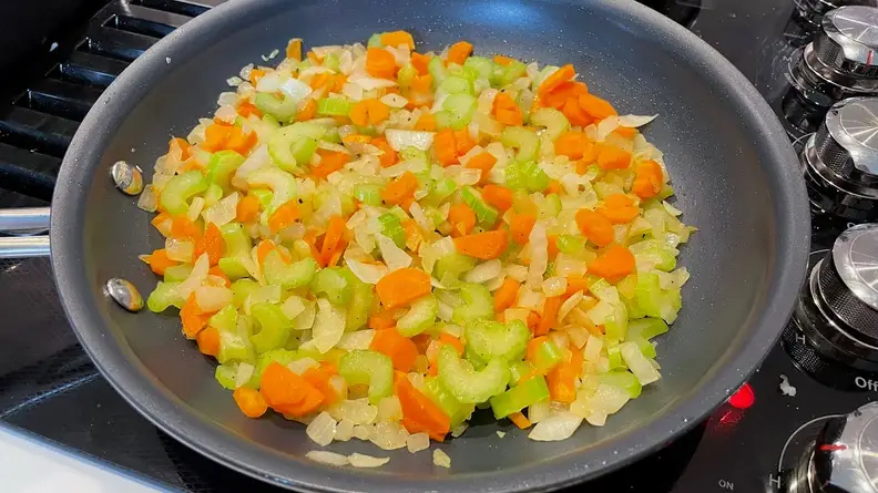 Assorted chopped vegetables cooking in a skillet on top of stove.