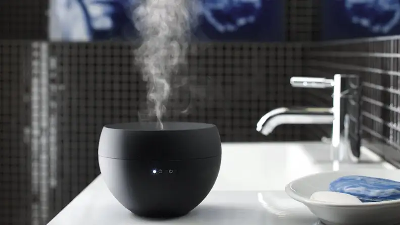 A black Stadler Form Jasmine essential oil diffuser sits on a bathroom sink.