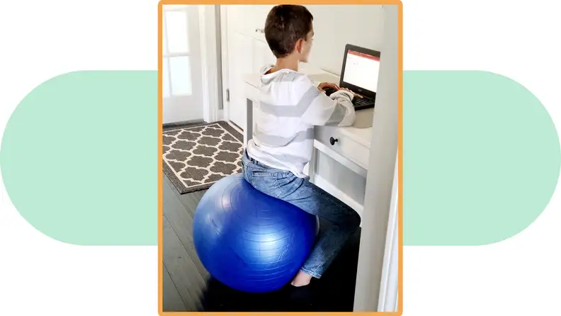 A child sits on a Urbn Exercise Ball while using a laptop.