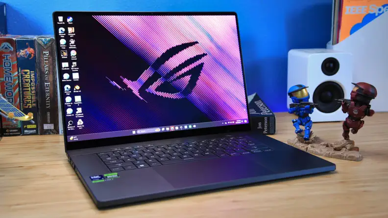 The laptop is on a wooden table in front of a blue wall.