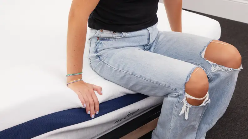 Person sitting on the edge of the  Helix Midnight mattress with both palms flat on mattress.
