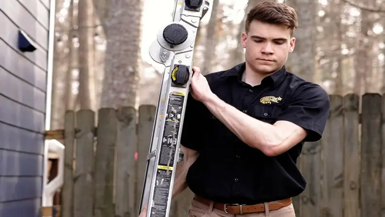 Technician carrying a ladder in a backyard near a fence