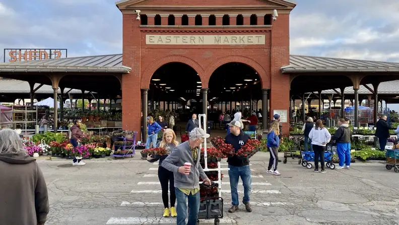 Shoppers with flower carts outside Eastern Market's brick entrance