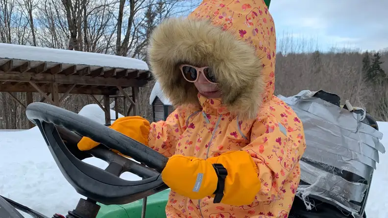 A child wearing the snowsuit while driving a snow car.