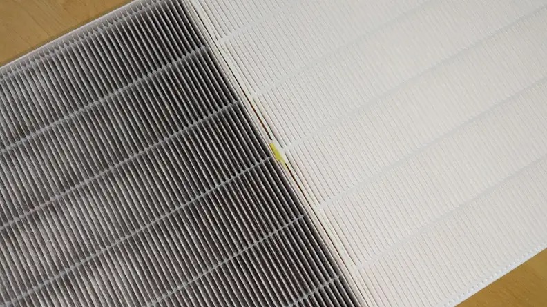 A used HEPA filter darkened by dirt and dust compared to a new clean filter.