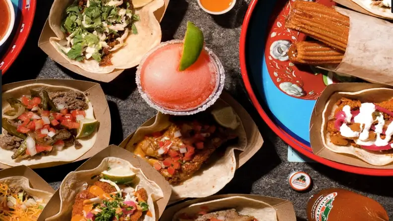 An overhead shot of assorted tacos, a margarita, and churros