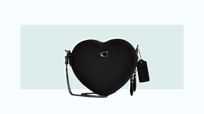 A black leather crossbody bag in the shape of a heart.