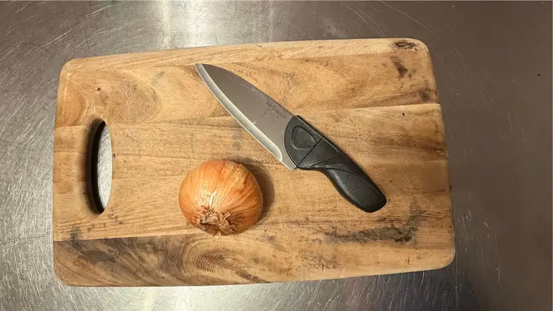 A knife and an onion on a wooden cutting board