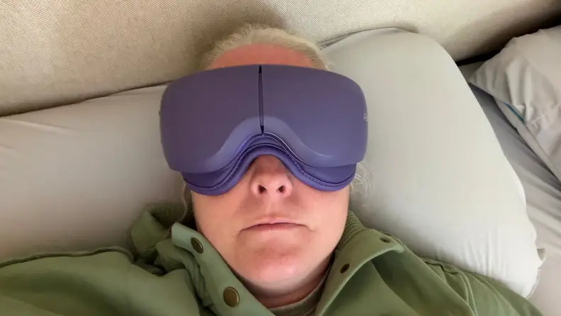 A woman lays against a pillow with a purple eyemask on