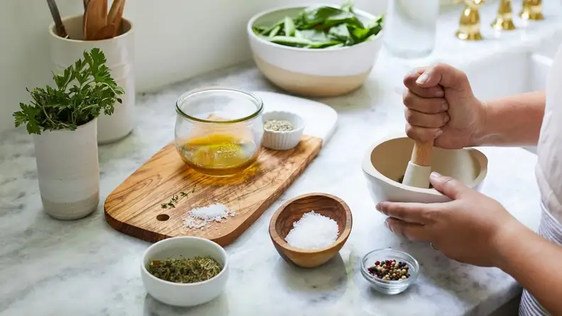 A hand grinding spices on a white marble countertop.