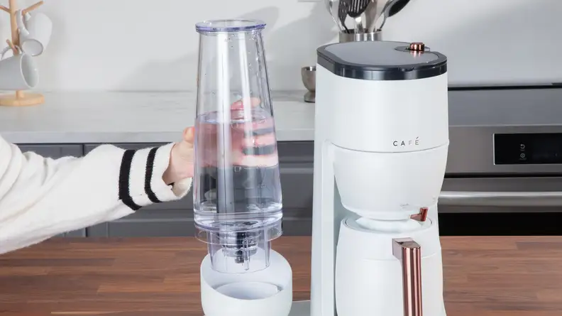 A person removing the water tank attached to the coffee machine in a kitchen.