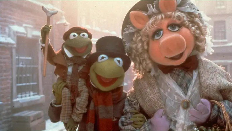 An ornately-dressed Miss Piggy (voiced by Frank Oz) and Kermit the Frog (voiced by Steve Whitmire) cary a Tiny Tim Cratchit frog (voiced by Jerry Nelson) down the cold city streets in 1992's The Muppet Christmas Carol