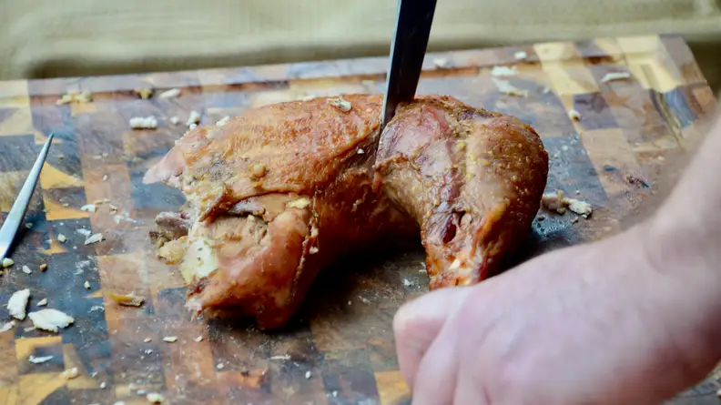A chef's knife cutting into a turkey thigh and leg.