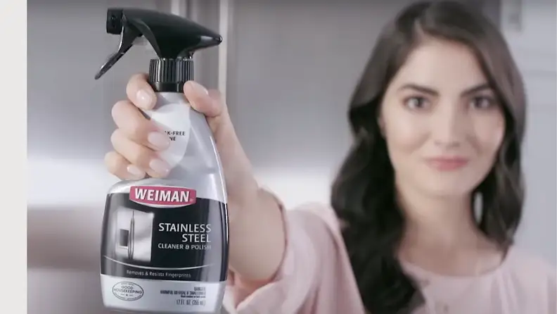 Weiman stainless steel cleaner spray focused on the image with a lady, blurred in the background, holding the cleaner
