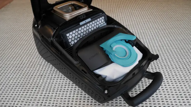 Miele Guard L1 Cat & Dog Vacuum opened up showing the inside of it with its filter and bag, on top of a white and grey rug.