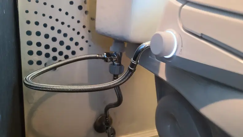 A closeup of the water line connector from the toilet to the bidet, and the control knob with backlight.