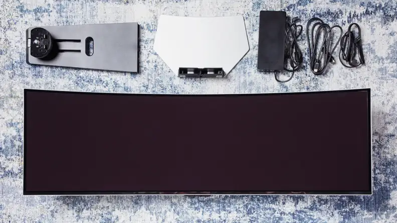 The Samsung Odyssey OLED G9 monitor on a rug next to other accessories for the Samsung Odyssey.