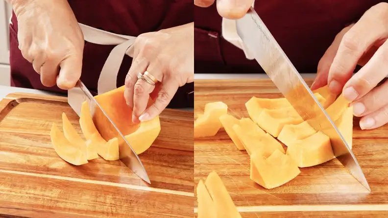Person using knife to cut butternut squash into spears and cubes on top of wooden cutting board.