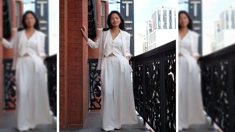 A woman on a balcony wearing a white linen suit with oversized pants and a matching vest.