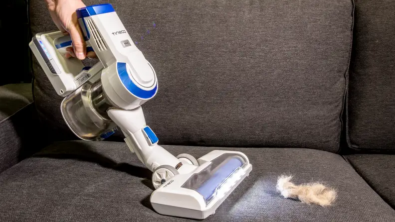 A close-up view of a person using the Tineco A10 vacuum to clean up pet hair on a grey sofa.