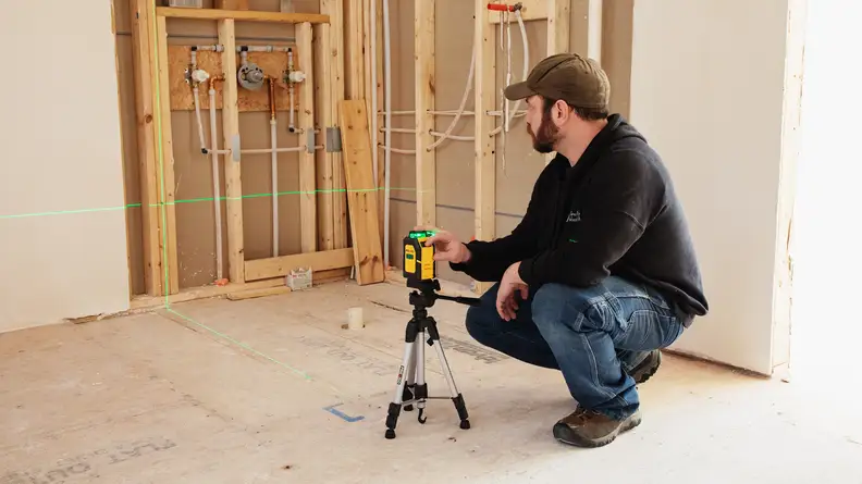A man crouches, setting up a Prexiso laser level.