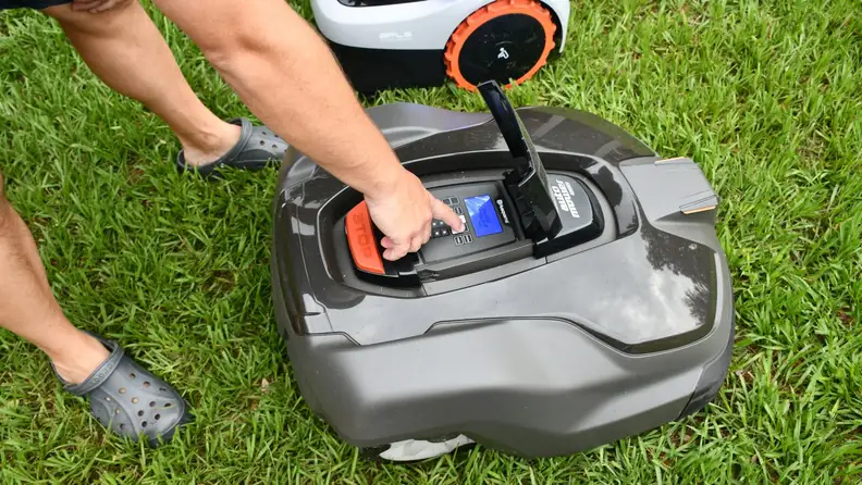 A person entering a passcode on the top of a robot lawn mower