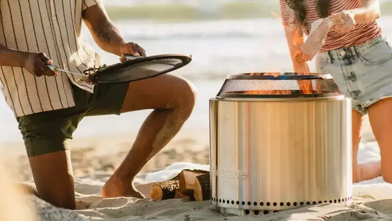 A couple using the Solo Stove Bonfire fire pit with accessories on a beach.