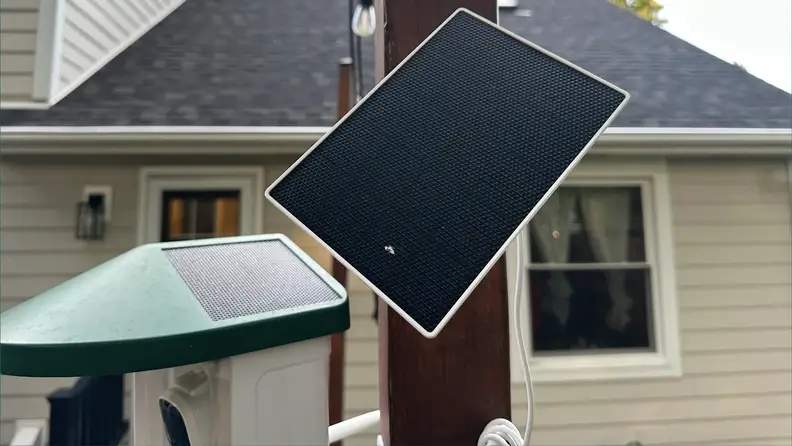 Sensor of Harymor Q8 Smart Birdfeeder mounted on pole in backyard in front of tan house.