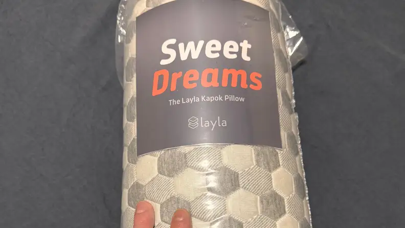 Layla Sleep Kapok Pillow shown rolled up in packaging against a dark grey background.