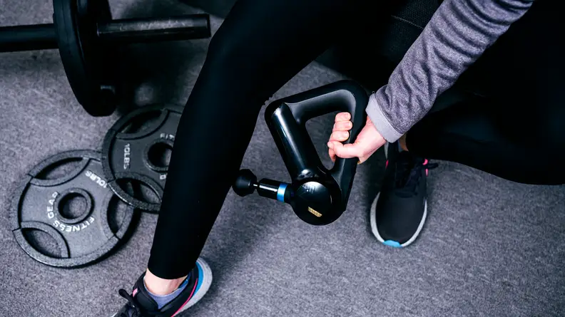 A Theragun Elite is used to massage a calf leg, and could be one of the best birthday gifts for Aries season.