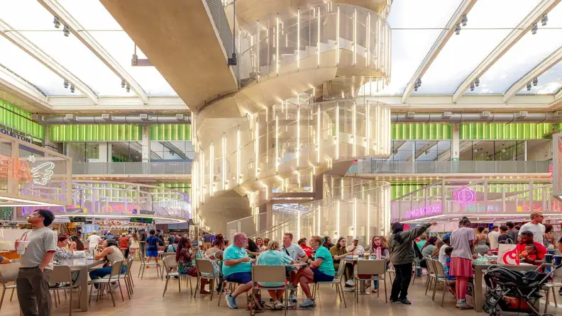 Glowing spiral staircase above a crowded food hall seating area